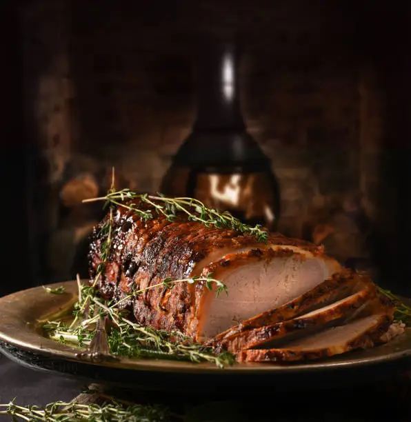 Creatively lit rolled pork roast with sage and thyme herb garnish shot against a rustic background with generous accommodation for copy space.