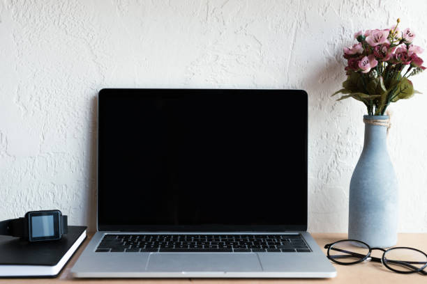 istock laptop with blank screen, smartwatch, notebook, eyeglasses and flowers in vase on table 1037679954