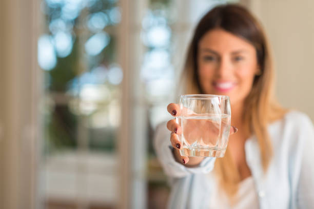 家庭での水のガラスを押しながら笑みを浮かべて美しい若い女性。ライフ スタイルのコンセプト。 - water women glass healthy eating ストックフォトと画像