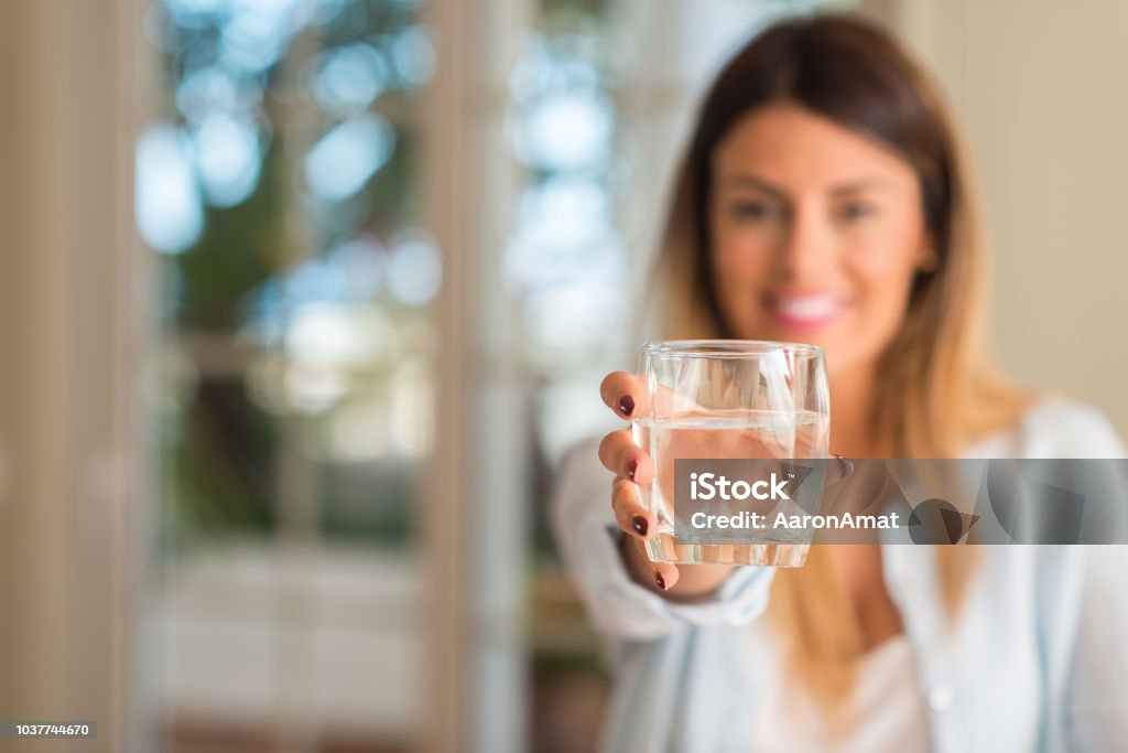 Beautiful young woman smiling while holding a glass of water at home. Lifestyle concept. Water Stock Photo