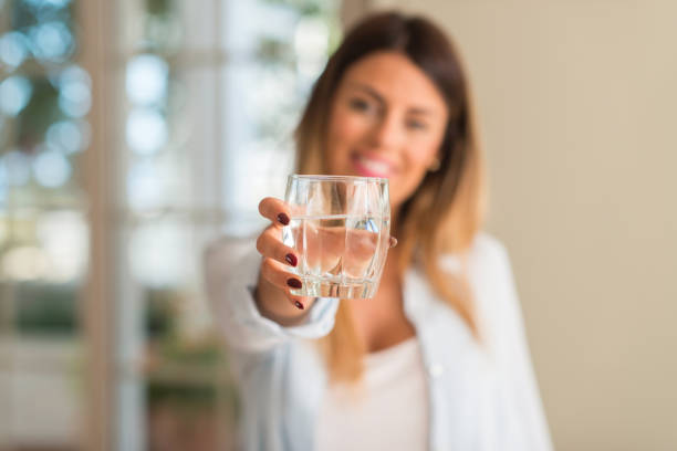 mooie jonge vrouw die lacht terwijl een glas water thuis. lifestyle concept. - drinking water stockfoto's en -beelden