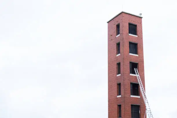 Tower for fire brigade emergency training practise and ladder against red brick facility and blank sky uk