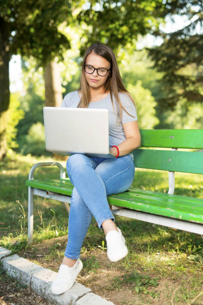 istock Young woman sitting on a bench outdoors in park and using laptop 1037835440