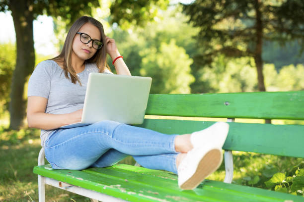istock Young woman sitting on a bench outdoors in park and using laptop 1037835510