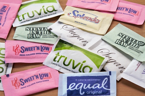 A group of various types of both artificial and natural sweeteners including Splenda, Sweet n Low, Equal, Truvia, Stevia in the Raw, and plain sugar. All items are in single serve paper packets.