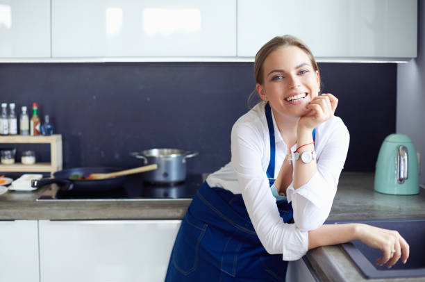 腕を組んでキッチンの背景に立っている若い女性の肖像画。 - stereotypical housewife women domestic kitchen brown hair ストックフォトと画像