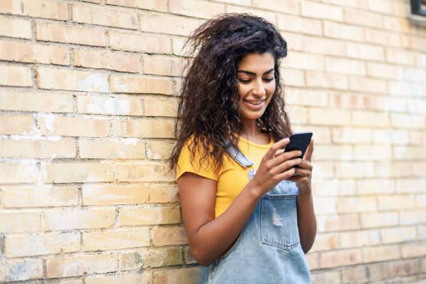 istock Happy Arab girl using smart phone on brick wall. 1037903534