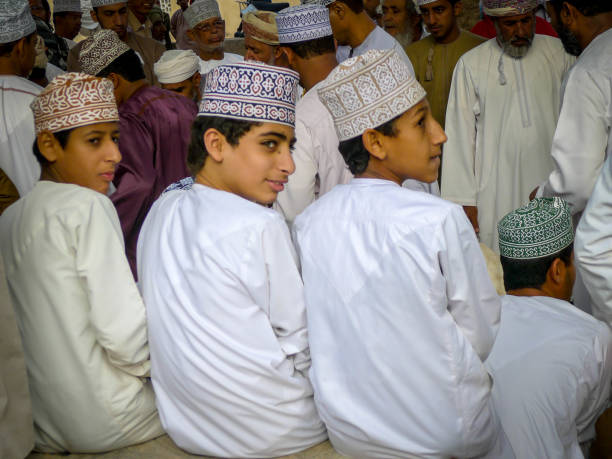 três jovens rapazes sentar-se em uma linha no mercado de cabra de domingo na cidade de nizwa nas montanhas hajar de omã - oman town arabia arabian peninsula - fotografias e filmes do acervo