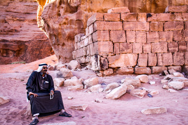 Bedouin man sitting in front of Lawrence's house in Wadi Rum, Jordan WADI RUM, JORDAN - Nov 2009: A bedouin man in traditional clothing sits next to the ruins of T E Lawrence's house in the UNESCO world heritage site of Wadi Rum in Jordan lawrence in arabia stock pictures, royalty-free photos & images
