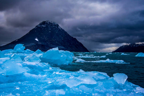 Blue sea ice with mountain and moody storm clouds, Svalbard, Norwegian Arctic Blue sea ice with mountain and moody storm clouds, Svalbard, Norwegian Arctic iceberg dramatic sky wintry landscape mountain stock pictures, royalty-free photos & images