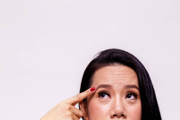 Asian young woman worried and pointing finger towards her aging and old forehead - with copy space - treatment skin care concept. stock photo