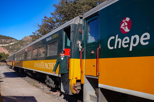 BAHUICHIVO, MEXICO - Jan 2016: A conductor leans out of the Chuhuahua-Pacifico (El Chepe) train at Bahuichivo railway station, in the Copper Canyon in northern Mexico