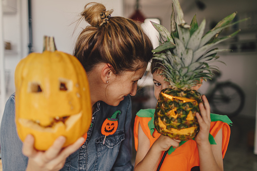 Mother and son holding a pumpkin and a pineapple over their faces on a Halloween