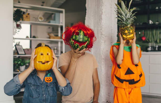 Halloween Family Family holding a watermelon, pineapple and a pumpkin over their faces on a Halloween carving fruit stock pictures, royalty-free photos & images