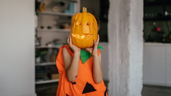Boy dressed as a pumpkin covering his face with a Jack O' Lantern on a Halloween