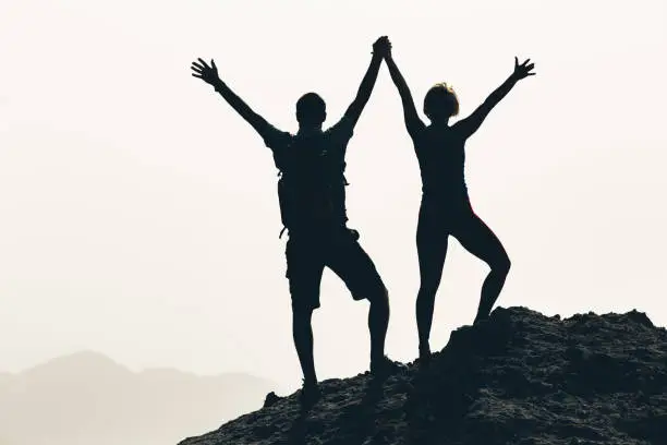 Successful couple achievement climbing or hiking, business concept with man and woman celebrating with arms up raised, outstretched outdoors. Motivational and inspirational silhouette landscape.