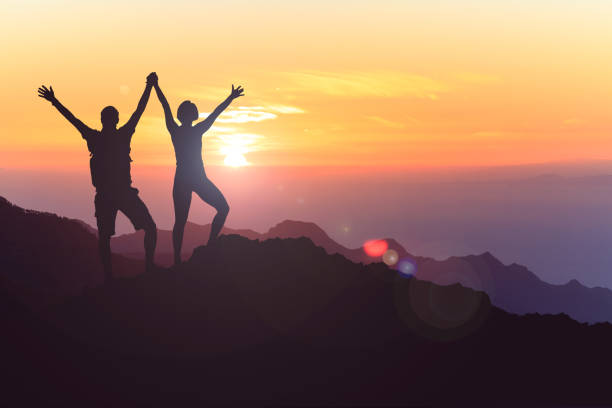 Happy couple celebrate, reaching life goal and success Successful couple achievement climbing or hiking, business concept with man and woman celebrating with arms up raised, outstretched outdoors. Motivational and inspirational silhouette landscape. arms outstretched photos stock pictures, royalty-free photos & images