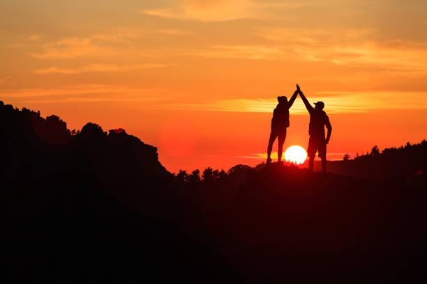 Teamwork couple celebrating in inspiring mountains sunset stock photo
