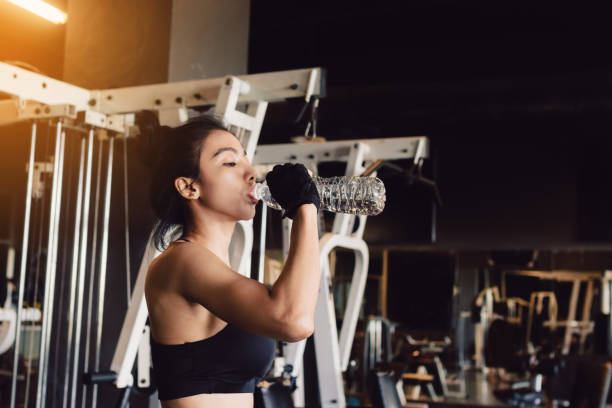 asiatique jeune femme l’eau potable dans le gymnase. - aerobics beautiful bottle body photos et images de collection