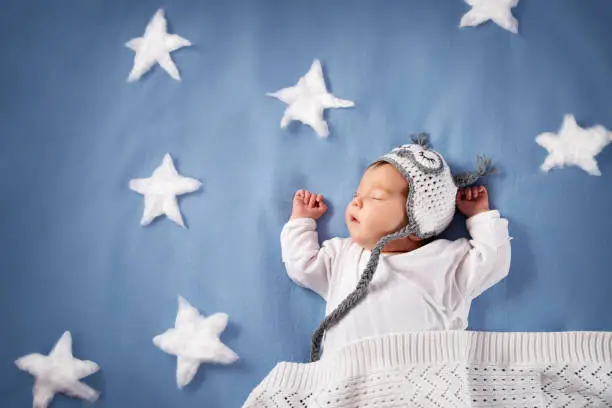 Photo of Cute newborn baby girl lying in the bed. 2 month old child in owl hat sleeping on blue blanket