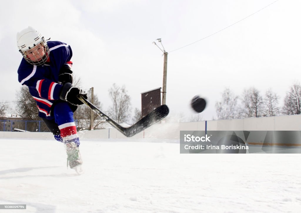 The boy plays hockey on a street skating rink.A boy on a skating rink plays hockey. Child Stock Photo