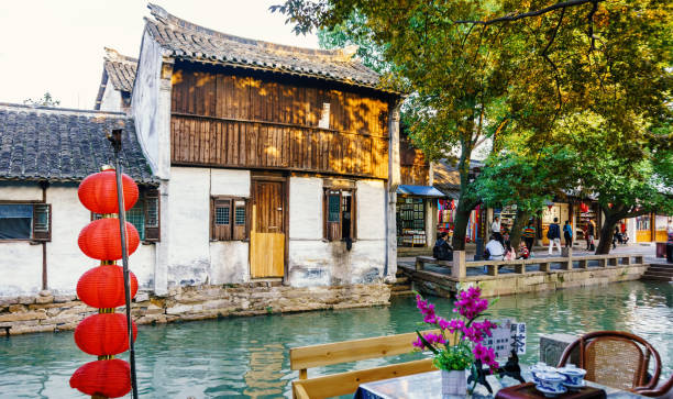 At the Zhouzhuang Water Town, Suzhou, China Suzhou, China - Nov 5, 2016: View across the waterway at the historic Zhouzhuang Water Town. Some visitors can be seen along the shoreline; some sitting down to relax, some walking. water town zhouzhuang china stock pictures, royalty-free photos & images