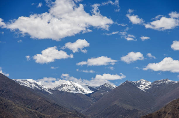 Desert hillside with bushes and tall barren mountains beyond under bright blue sky.
