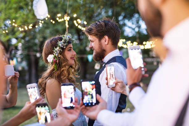 clientes con smartphones tomando foto de novios en el banquete fuera. - men groom wedding red fotografías e imágenes de stock