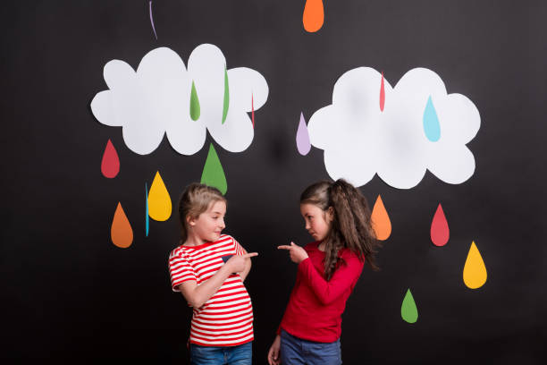 istock Small girls in studio, standing against black background with clouds and raindrops. 1038177852