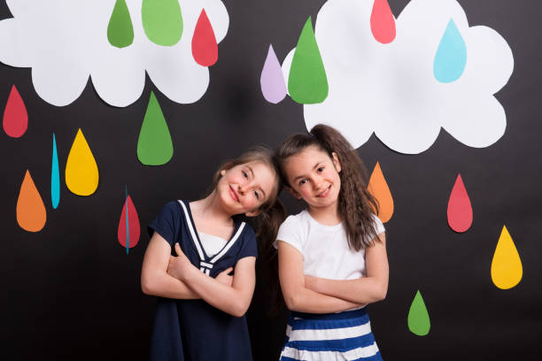 istock Small girls in studio, standing against black background with clouds and raindrops. 1038179108