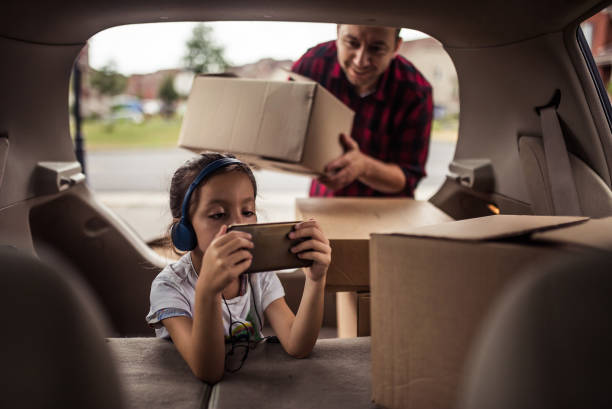 Little girl playing and listening to music in the trunk of the car while her father is loading moving boxes Little girl playing and listening to music in the trunk of the car while her father is loading moving boxes into the car. View from inside the car real life photos stock pictures, royalty-free photos & images