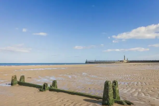 Photo of Whitby beach with breakwater and pier.