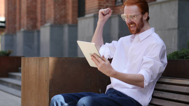 istock Excited Man Celebrating Success on Tabletp Sitting on Bench 1038202400
