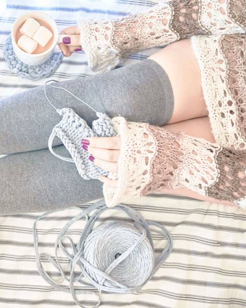 A woman on the bed knits a scarf.