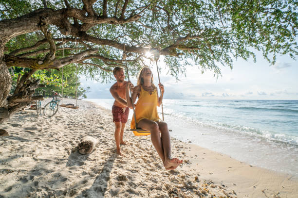 istock Young man pushing girlfriend on swing by the beach at sunset enjoying romantic tropical vacations 1038256882