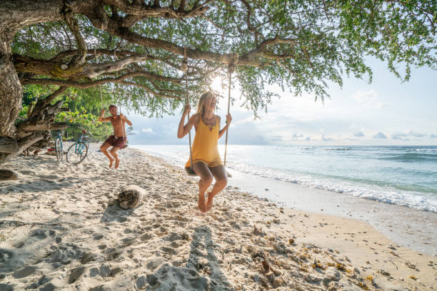 Two young adults playing on swing on the beach in tropical paradise, couple having fun happy sharing beautiful moments in perfect vacation time in Asia Young couple swinging over the sea, beautiful and idyllic landscape. People travel romance vacations concept. gili trawangan stock pictures, royalty-free photos & images