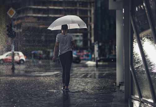 Rear view of a woman with umbrella walking on the street during rainy day.