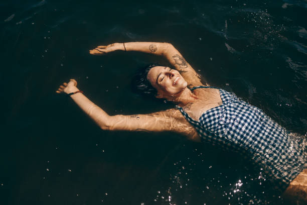 Smiling woman on a holiday relaxing by swimming in lake. Woman in bikini floating in water facing up.