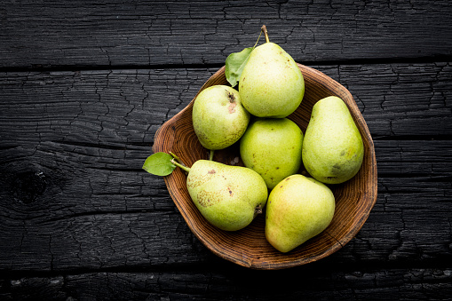 Pears in wooden bowl on dark wooden background