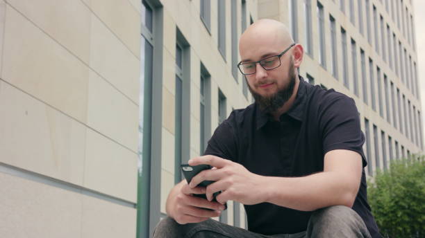 istock Man with Beard Wearing Glasses Using a Phone in Town 1038364574