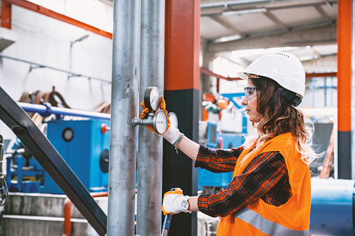 Portrait of a serious technician or engineer woman checking pressure device for industry system, opening or closing valve equipment in industrial site factory or utility.