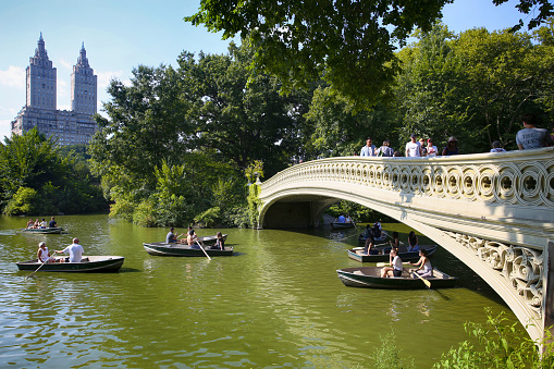 New York, USA - August 24, 2018: View of the Bow Bridge and people taking a boat ride in Central park, New York, Bow bridge was built between 1859 and 1862.