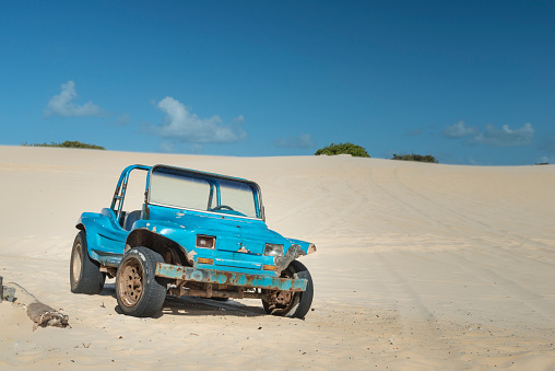 1970s old abandoned buggy car on natal sand dunes. Blue paint rusted, missing headlight, cracked windshield bugre on a sandy area of Natal, Rio Grande do Norte.