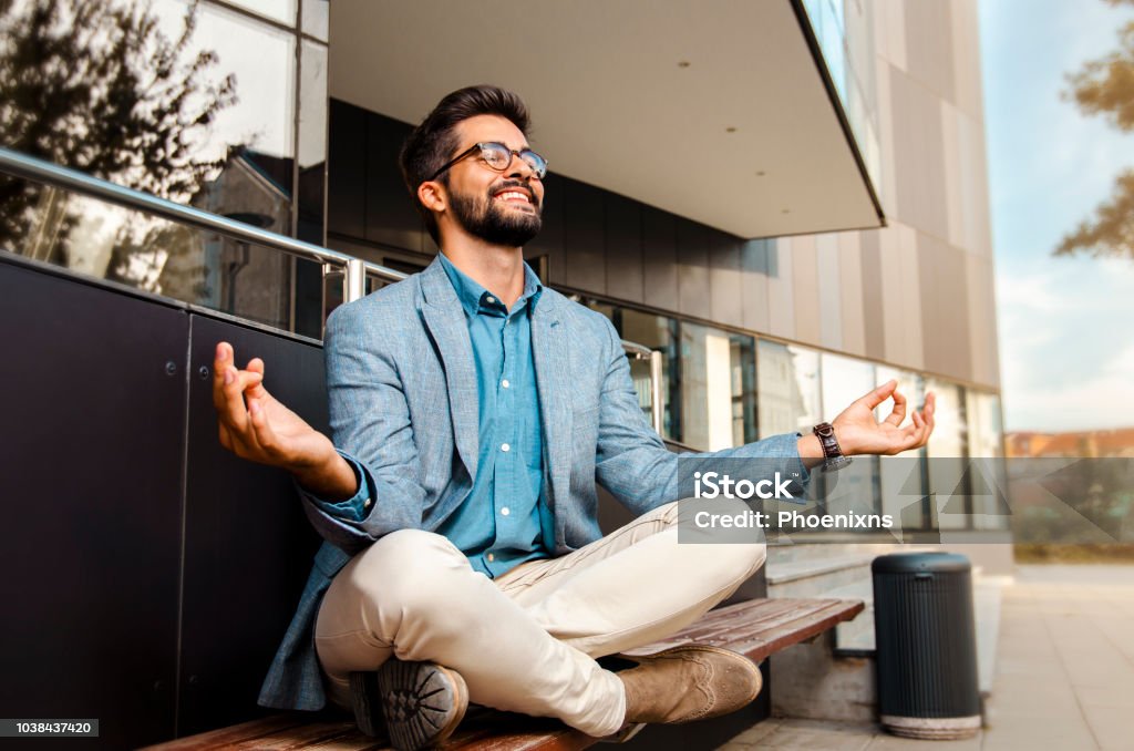 Businessman - mentally preparing for business meeting. Businessman - mentally preparing for business meeting. Sitting in meditation pose in front of office building and smiling Working Stock Photo