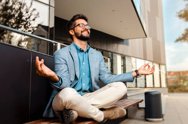 Businessman - mentally preparing for business meeting. Businessman - mentally preparing for business meeting. Sitting in meditation pose in front of office building and smiling Mentally stock pictures, royalty-free photos & images