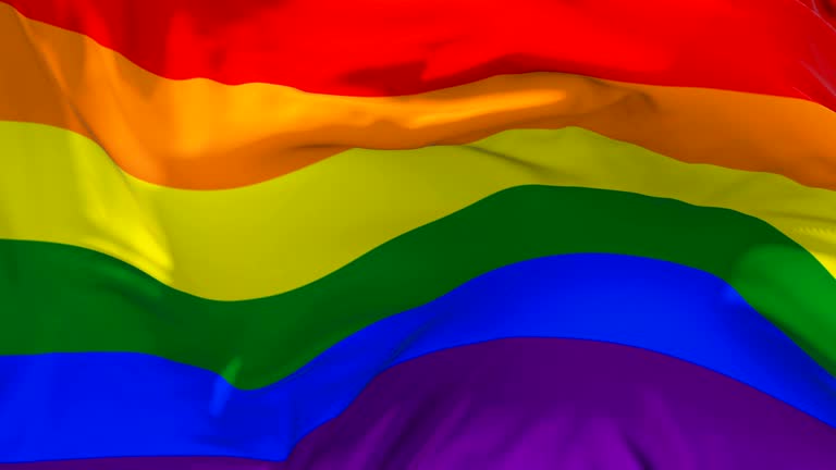 Gay Pride Rainbow Flag Waving in Wind Slow Motion Animation . 4K Realistic Fabric Texture Flag Smooth Blowing on a windy day Continuous Seamless Loop Background.