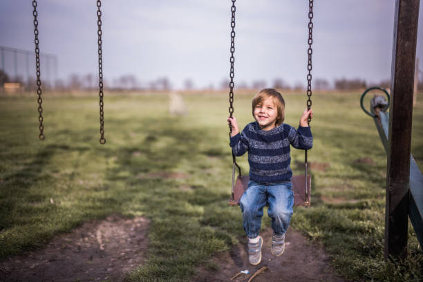istock Happy small boy swinging in nature and looking at camera. 1038596968