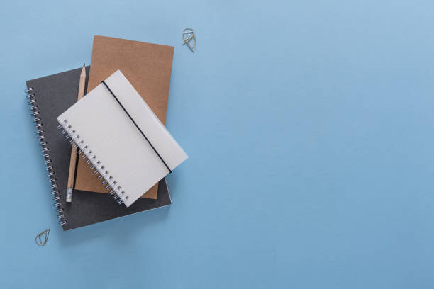 istock Top view over the working desk with notebook, pencil and paper clips. Copy space for text. Flat lay of a workplace on blue background 1038612046
