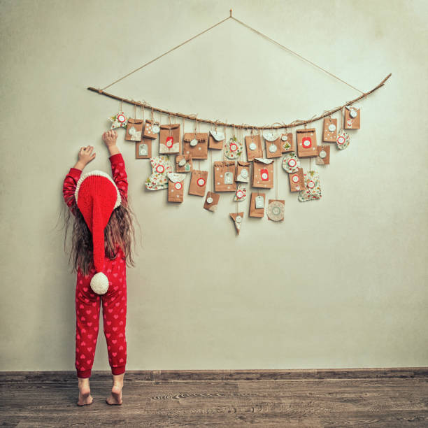 enfant en pyjama et bonnet de noël s’étend sur le calendrier de l’avent avec des petits cadeaux. kid compte jours jusqu’au nouvel an - advent calendar christmas number red photos et images de collection