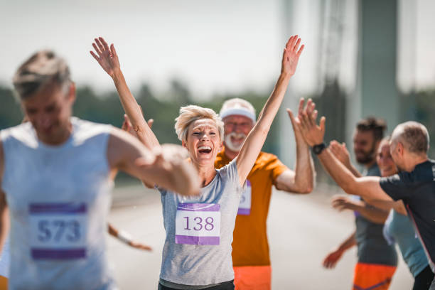 Happy senior woman celebrating her end of marathon race. Happy mature woman celebrating the end of marathon race after greeting with her supporters and looking at camera. finish line photos stock pictures, royalty-free photos & images